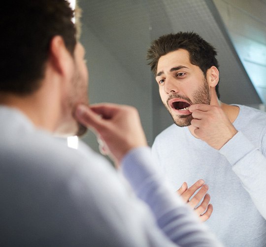 a man looking at his teeth in a bathroom mirror