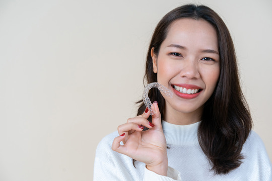 woman smiling while holding Invisalign aligner